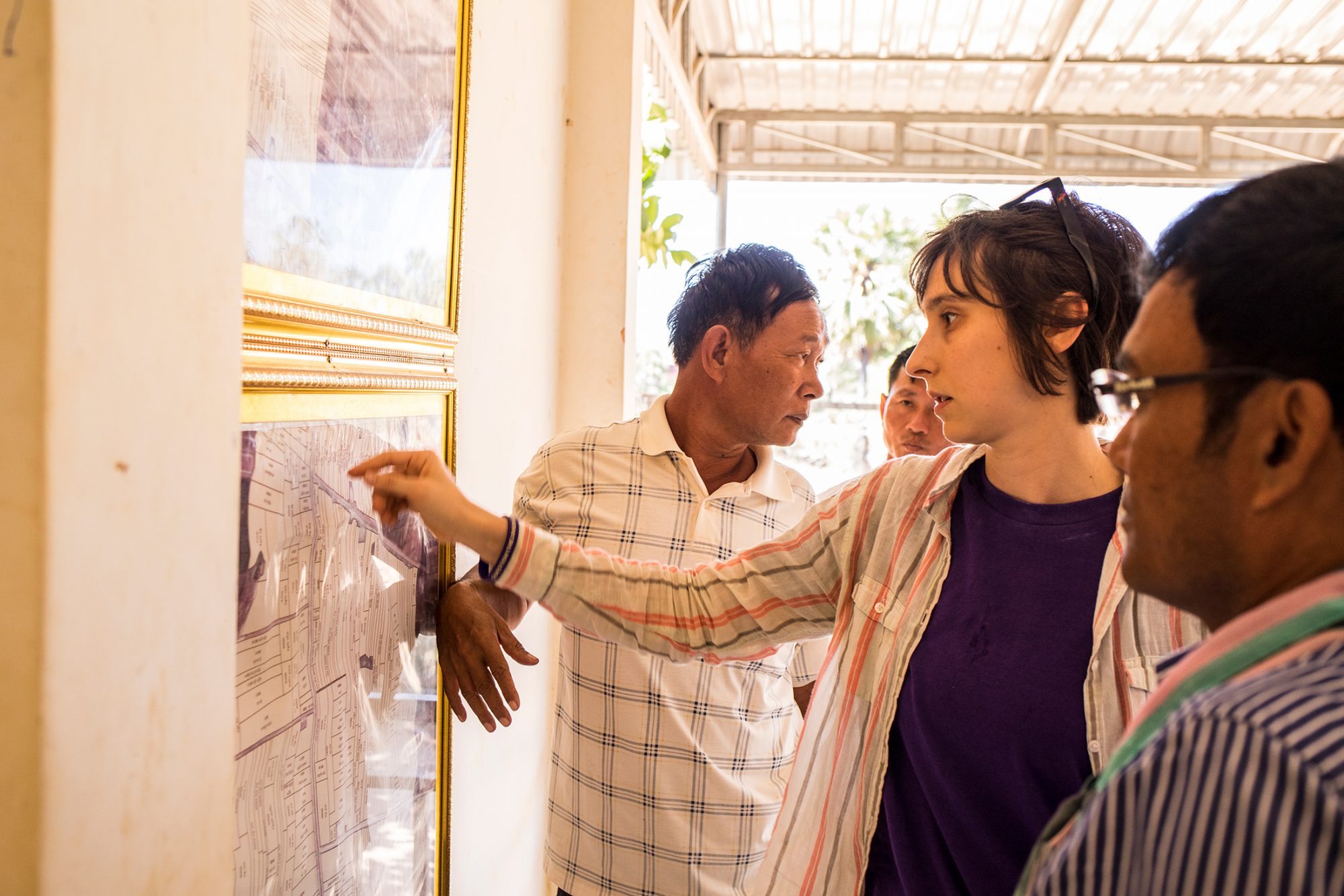 Three Cambodian farmers and Yasmine gather around a faded purple map posted on the wall