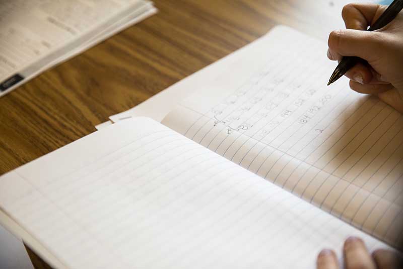 A persons hand, writing in a notebook.