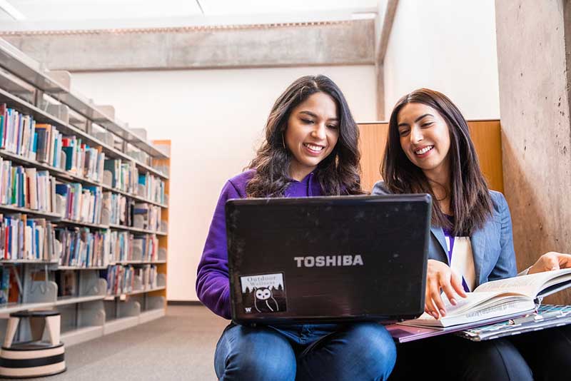Two students sitting next to each other looking at a laptop.