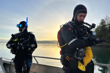 two people in scuba gear prepare to dive from a boat