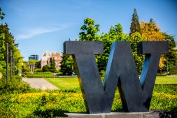a university of washington 'W' statue with grass and buildings beyond